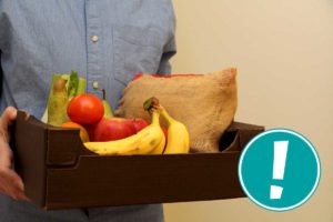 Eine Person hält eine Kiste mit frischem Obst und Gemüse.