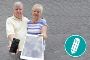 Ein älteres Pärchen hält ein Smartphone und ein Tablet in die Kamera.
