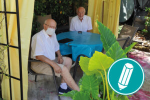 Zwei Senioren sitzen im unter einem Pavillon und schauen auf ihr Smartphone und Tablet.