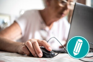 Eine ältere Frau sitzt vorm Laptop und klickt mit der Maus.