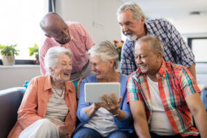 Fünf Senior*innen schauen auf den Bildschirm eines Tablets und lachen