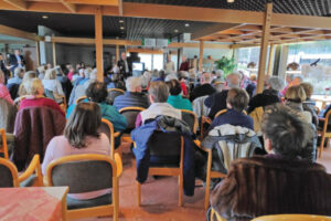 Der Raum ist gefüllt mit über 80 Personen. Die Menschen schauen nach vorne, wo die DigiBos sich vorstellen.