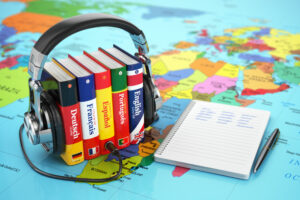 Kopfhörer auf Lexiken stehen auf einer Weltkarte, daneben ein beschriebener Block mit Stift