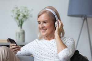 eine ältere Frau schaut lächelnd auf ihr Handy und trägt Kopfhörer