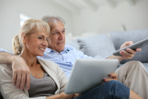 ein älteres Paar sitzt mit Laptop und Fernbedienung auf der Couch