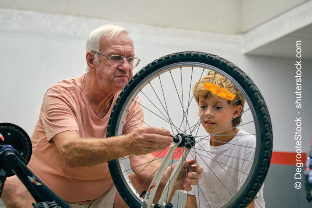Ein Opa zeigt seinem Enkel, wie man ein Rad am Fahrrad wechselt.