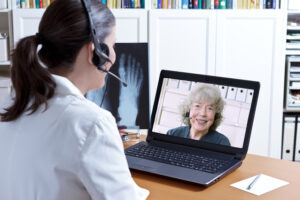 Ärztin sitzt mit Kopfhörern an einem PC und berät digital eine Frau.