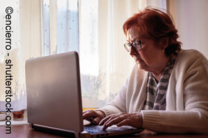 Eine ältere Frau sitzt vor dem Laptop und schaut überrascht.