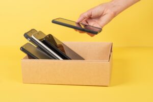 Eine Hand legt ein Smartphone in eine Schachtel mit weiteren Smartphones.