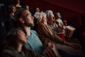 Mature couple enjoying while eating popcorn and watching a movie i cinema. Focus is on woman.