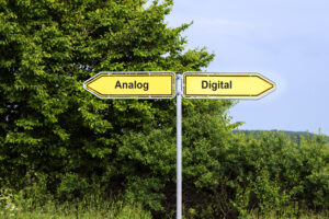 Yellow road signs pointing in opposite directions with text Analog, Digital, green bushes and a blue sky in the background, symbol concept for future-oriented technology