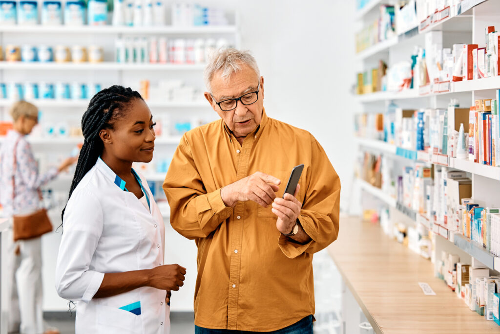 Ein Apothekerin zeigtihrem Kunden etwas auf seinem Smartphone in einer Apotheke